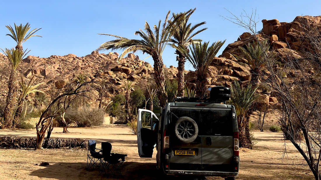 Grey campervan with palm trees and rocky hills in Tafraoute Morocco