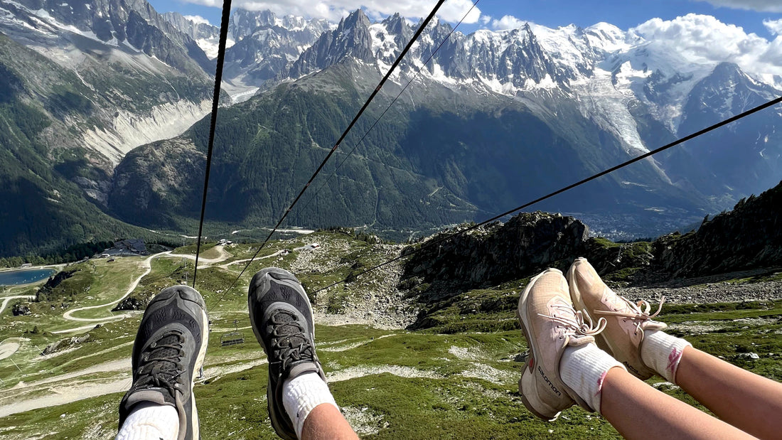 Two pairs of feet in the air on a cable car with Mont Blanc massif in the background