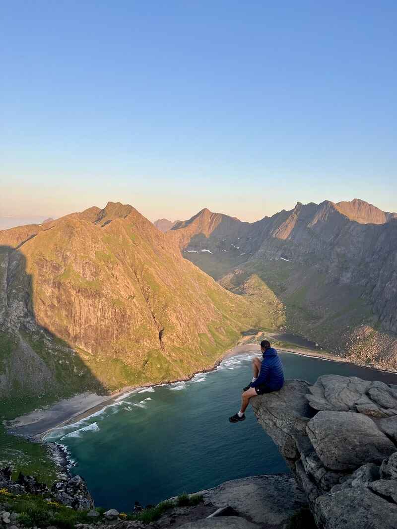 man sitting on the edge of a rock overlooking a beach and mountains